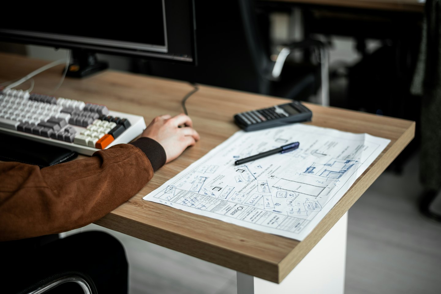 Designer che lavora a piani architettonici e wireframe UI su una scrivania.