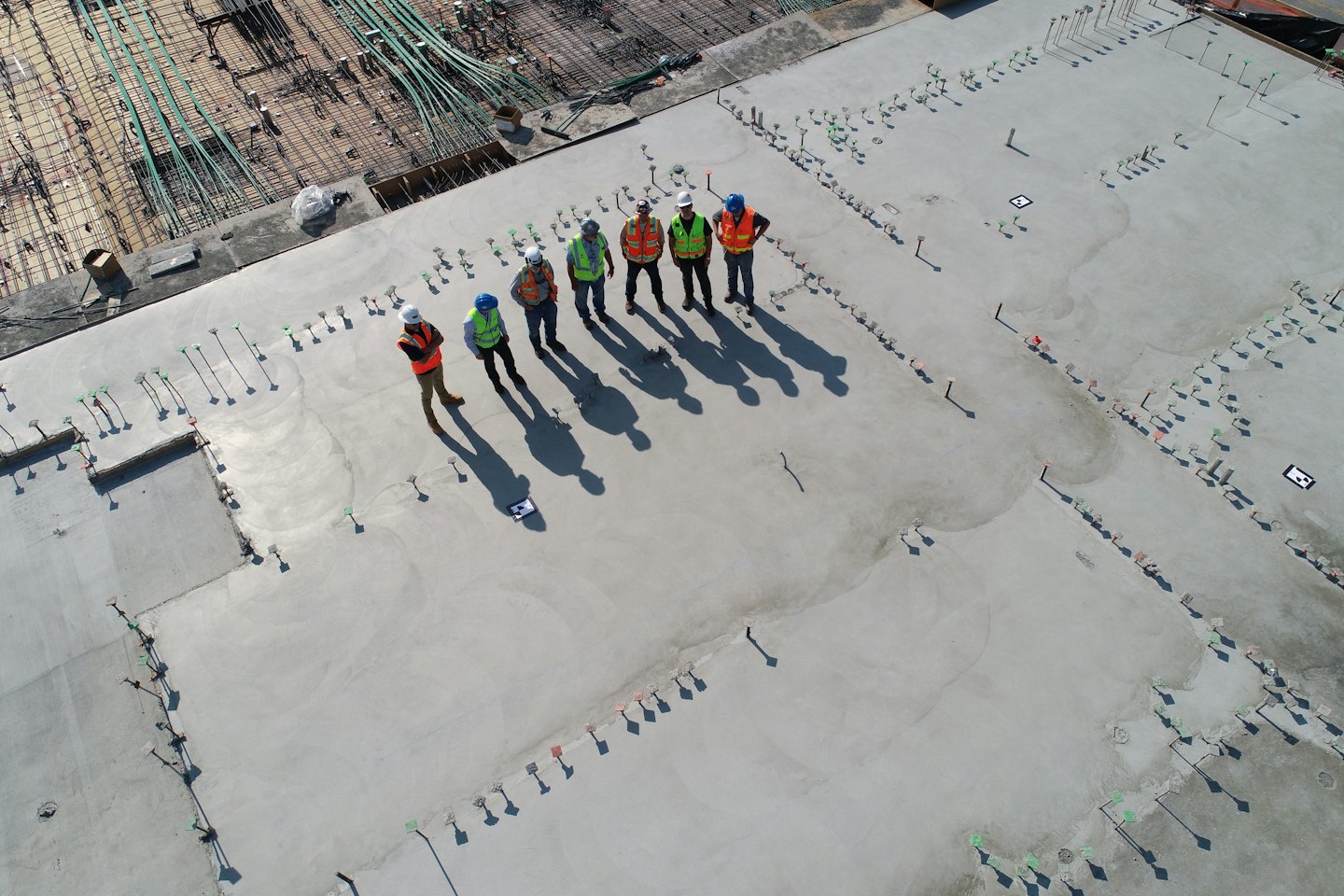 Operai edili con giubbotti ispezionano un cantiere in cemento grezzo.