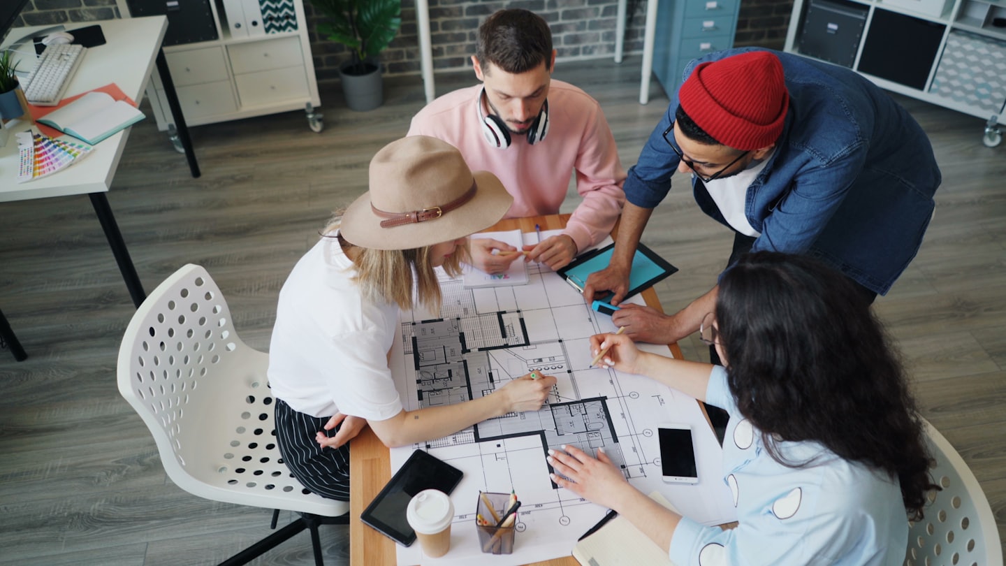 Quattro adulti discutono progetti su un tavolo di legno.